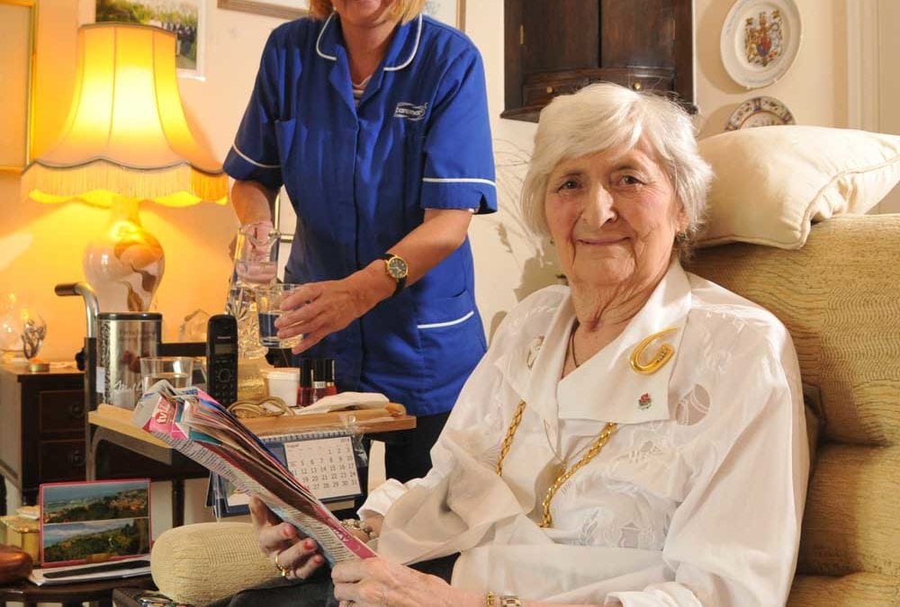 Elderly woman smiling at camera as care assistant pours drink